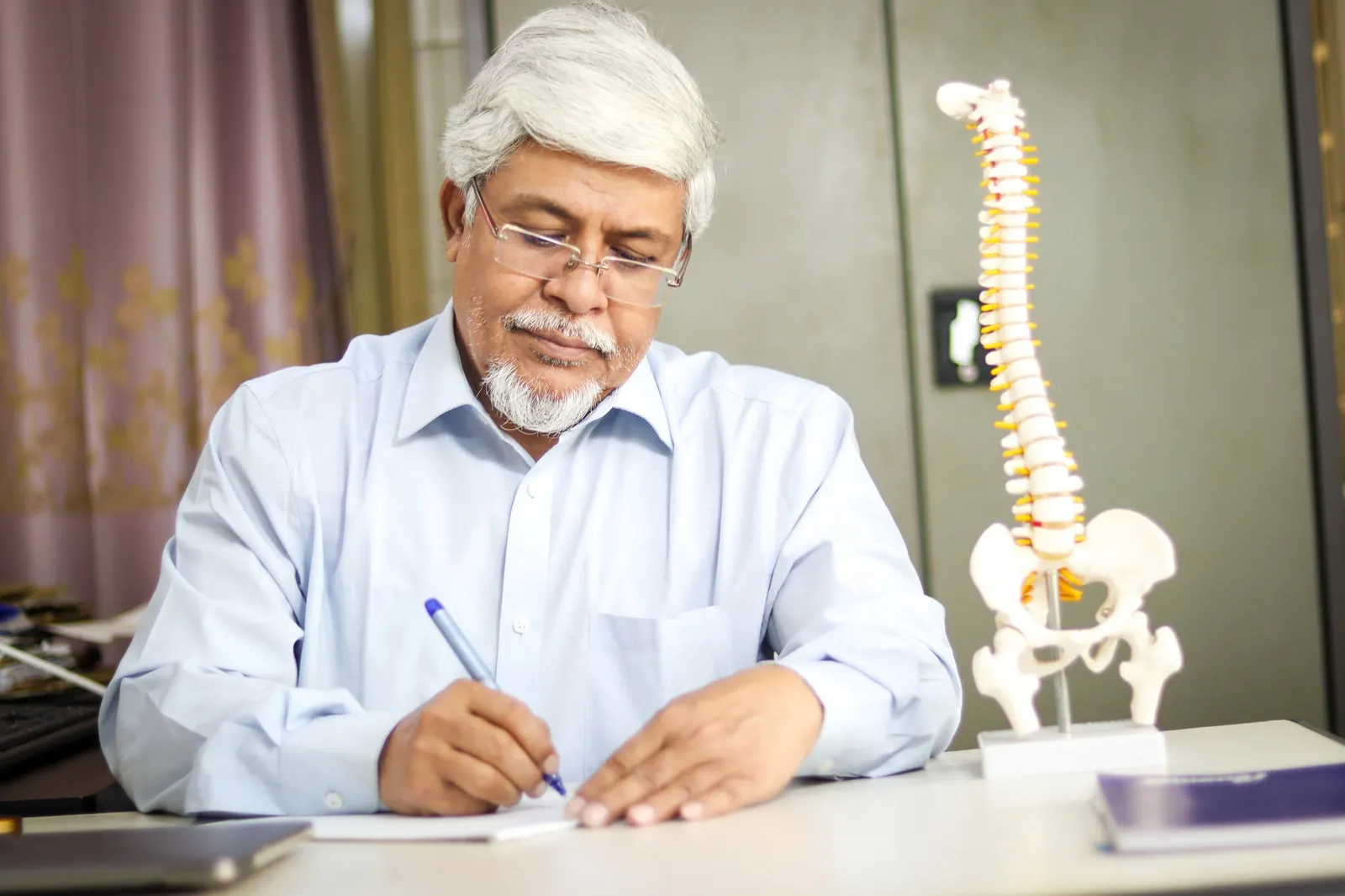 Prof. Dr. Md. Kamrul Ahsan, spine surgeon in Dhaka, at his desk beside a spine model